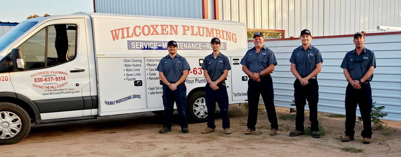 Five Wilcoxen Plumbing plumbers in uniform shirts and caps standing in front of a white service truck